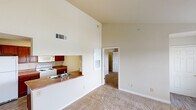 Located at 9260 S 73rd W Ave in Sapulpa, Oklahoma, this single-story home offers a functional and open layout with several notable architectural details. The living area is anchored by striking vaulted ceilings that lend a sense of spaciousness and airiness to the space. Soft carpeting covers the living and bedroom areas, while wood-look flooring runs through the kitchen and bathrooms. A pass-through counter connects the living area to the kitchen, maintaining an open feel between the two spaces. The kitchen is equipped with rich dark wood cabinetry, laminate countertops, a white electric range, microwave, and refrigerator, all accented by overhead fluorescent lighting. The living room features multiple windows fitted with blinds and a glass door providing access to an outdoor area, allowing natural light to fill the room. Bedrooms are carpeted and each includes a window with blinds; one bedroom features a ceiling fan with light fixture. The bathrooms are finished with matching dark wood vanity cabinets, laminate countertops, large mirrors, and wood-look flooring. One bathroom includes a soaking tub and an additional wall-mounted storage cabinet, while the other offers a tub-shower combination. Overall, the home presents a clean, neutral palette throughout.