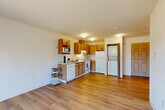Located at 9615 Holly Dr in Everett, WA, this one-bedroom, one-bathroom unit offers a thoughtfully laid-out single-floor living space. The open-plan kitchen and living room form the heart of the home, bathed in natural light from a sliding glass door that leads directly to a private balcony with pleasant outdoor views of surrounding greenery. The kitchen is well-equipped with warm oak cabinetry, ample counter space, a double sink, electric range, dishwasher, and a full-size refrigerator. A stacked washer and dryer unit is conveniently housed within the kitchen area, adding in-unit laundry functionality. The living room features smooth hardwood-style flooring that extends throughout the main area, creating a clean and cohesive aesthetic. The bedroom is carpeted for comfort, featuring a window with natural light, a baseboard heating system, and access to two closets providing generous storage. The bathroom is equipped with a full soaking tub and grab bars, adding a practical and accessible touch. Neutral tones, clean walls, and a straightforward layout make this a versatile and functional living space suitable for a range of lifestyles.
