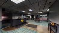 Match Point Tennis and Fitness Club in Griffith, Indiana is a well-appointed single-floor recreational facility designed to serve both competitive and casual athletes. Visitors are greeted at the entrance by a sleek, dark reception desk prominently displaying the club's gold "MP" logo, setting a professional and spirited tone from the moment of arrival. The flooring throughout the common areas features a distinctive plaid carpet in muted teal and green tones, providing a cohesive and inviting aesthetic across the space.

A windowed corridor runs alongside the indoor tennis courts, furnished with high-top bar tables and stools, offering members a comfortable vantage point to watch play in action. Large windows along this gallery-style hallway ensure visual connectivity between the social areas and the courts below.

The club also features a well-equipped lounge area with leather sectional seating, a wall-mounted flat-screen television, a popcorn machine, and built-in cabinetry with a beverage refrigerator — ideal for relaxing before or after a session. A secondary lounge space includes additional leather seating, a coffee station, under-counter refrigeration, and framed artwork, creating a cozy retreat for members.

Throughout the facility, tasteful tennis-themed décor, including a framed vintage racket display, reinforces the club's identity. A drop-panel ceiling with recessed and track lighting maintains a clean, functional look across all areas of the club.