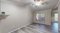 This single-story residence offers a thoughtfully designed layout that balances comfort and functionality. Throughout the home, light gray hardwood-style flooring provides a clean, cohesive aesthetic, while crown molding and textured ceilings add a classic architectural touch. Ceiling fans are present in every room, contributing to year-round comfort.

The living area is a standout space, featuring vaulted ceilings that create an open, airy feel, along with a white-mantled fireplace that serves as an attractive focal point. Natural light filters in through blinds-fitted windows, enhancing the warm, neutral color palette of the walls.

The kitchen is well-equipped with warm honey-toned cabinetry, a tile backsplash, light quartz-style countertops, and stainless steel appliances including a gas range and microwave. A breakfast bar connects the kitchen to the adjacent living space, making it ideal for casual dining and entertaining.

The bedrooms are generously proportioned, with vaulted or standard ceilings, ample natural light, and dedicated closet space. One bedroom features mirrored sliding closet doors for added functionality.

The bathroom includes a wooden-framed vanity mirror, a single-basin sink with quartz-style countertops, and in-unit laundry access, adding significant convenience to daily living.