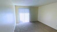 This single-floor space offers a clean, straightforward layout designed for comfortable everyday living. The main living area is a standout feature, characterized by its generous open floor plan, plush wall-to-wall carpeting in a neutral tone, and soft yellow walls that create a warm, inviting atmosphere. A large sliding glass door serves as the focal point of the room, fitted with vertical blinds that allow for adjustable natural light throughout the day. When fully illuminated, the room is bathed in bright, diffused light, enhancing the sense of openness and space. The textured ceiling adds a classic architectural touch, while the clean white trim and baseboards provide a crisp contrast to the warm wall tones. The overall ambiance of the space is calm and neutral, offering a versatile canvas well-suited for a variety of interior styles and furnishing arrangements. The single-floor layout ensures ease of accessibility and flow throughout the space, making it practical and functional for daily use.
