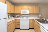 Located at 2501 Fairfax Rd in Greensboro, North Carolina, this single-floor unit offers a practical and comfortable layout designed for everyday living. The living areas are finished with neutral-toned wall-to-wall carpeting and warm beige walls, creating a cohesive and inviting atmosphere throughout. Textured ceilings add a classic touch, and ceiling fans in key rooms provide year-round comfort and air circulation.

The spacious living room benefits from abundant natural light through a large multi-pane window, making the room feel open and airy. The bedrooms are generously sized, each featuring ceiling fans with light fixtures and ample wall space. One bedroom connects directly to an adjoining room, offering flexible use of space.

The kitchen is efficiently designed with light wood cabinetry, white appliances including a refrigerator, electric range, and built-in microwave. A peninsula with a double stainless steel sink and white countertops opens to the adjacent living area, creating a convenient pass-through layout ideal for casual dining and entertaining.

The bathroom is outfitted with a full-size soaking tub and shower combination, light wood vanity cabinetry, and tile flooring. Clean white finishes throughout the bath contribute to a bright, functional space. Overall, the unit presents a straightforward, well-organized floor plan suitable for comfortable residential living.