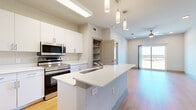 This thoughtfully designed one-bedroom, one-bathroom residence offers a cohesive open-concept layout finished with warm light wood flooring throughout. The kitchen serves as the centerpiece of the living area, featuring crisp white cabinetry extending to the ceiling for ample storage, a suite of stainless steel appliances including a range and microwave, and a peninsula island with a quartz countertop and undermount sink — ideal for both meal preparation and casual dining. Pendant lighting above the island adds a modern accent. The open living area flows naturally toward a sliding glass door that leads to a private balcony, offering scenic outdoor views and filling the space with natural light. A ceiling fan enhances comfort throughout the common area. The bedroom is a comfortable, well-proportioned retreat with large windows framing open landscape views, a ceiling fan, and direct access to a dedicated closet. The bathroom is cleanly appointed with an extended vanity, quartz countertop, undermount sink, and a wide mirror illuminated by overhead lighting. An in-unit washer and dryer area is also present. Neutral tones and modern hardware throughout give the space a fresh, contemporary feel.