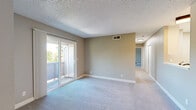 Located in Auburn, CA, this single-floor, two-bedroom residence offers a practical and comfortable layout with a clean, neutral aesthetic throughout. The galley-style kitchen is well-appointed with white shaker cabinetry, light countertops, a stainless steel sink, gas range, refrigerator, and overhead microwave, all set over light wood-look vinyl flooring that lends a bright, modern feel. The combined kitchen and living area transitions into a carpeted living room filled with natural light, featuring a sliding glass door that opens to a private balcony with views of surrounding greenery. A ceiling fan adds comfort to the adjoining space, which also features durable wood-look flooring. The generously sized primary bedroom is carpeted and includes an en-suite vanity area with a large mirror and built-in counter, along with an additional door providing further access. The second bedroom is equally well-sized, finished with plush carpet, neutral taupe walls, a textured ceiling, and a window with vertical blinds that invite natural light. Sliding panel closet doors are featured in one of the bedrooms, while a dedicated walk-in closet with dual clothing rods and shelving provides excellent storage. Throughout the residence, consistent neutral tones and textured ceilings create a cohesive, understated ambiance.