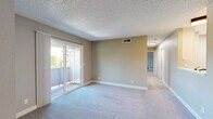 Located in Auburn, CA, this single-floor, two-bedroom residence offers a practical and comfortable layout with a clean, neutral aesthetic throughout. The galley-style kitchen is well-appointed with white shaker cabinetry, light countertops, a stainless steel sink, gas range, refrigerator, and overhead microwave, all set over light wood-look vinyl flooring that lends a bright, modern feel. The combined kitchen and living area transitions into a carpeted living room filled with natural light, featuring a sliding glass door that opens to a private balcony with views of surrounding greenery. A ceiling fan adds comfort to the adjoining space, which also features durable wood-look flooring. The generously sized primary bedroom is carpeted and includes an en-suite vanity area with a large mirror and built-in counter, along with an additional door providing further access. The second bedroom is equally well-sized, finished with plush carpet, neutral taupe walls, a textured ceiling, and a window with vertical blinds that invite natural light. Sliding panel closet doors are featured in one of the bedrooms, while a dedicated walk-in closet with dual clothing rods and shelving provides excellent storage. Throughout the residence, consistent neutral tones and textured ceilings create a cohesive, understated ambiance.
