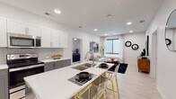 Located at 4001 Dr. Martin Luther King Jr. Blvd in Kansas City, MO, this single-floor unit showcases a clean, contemporary design with an open-concept layout that connects the kitchen and living areas seamlessly. The kitchen is well-appointed with two-tone cabinetry — white upper cabinets paired with gray lower cabinets — complemented by a tiled backsplash, stainless steel appliances including a refrigerator, range, and microwave, and a large center island with a built-in sink and seating. Light wood-style flooring runs throughout the main living areas, enhancing the bright, airy atmosphere created by recessed lighting and large windows dressed with sheer curtains. The living room offers a comfortable, open setting with natural light and a neutral color palette. The bedrooms feature plush carpeting and ceiling fans, with one bedroom providing direct access to a full bathroom. The bathrooms are finished with large-format tile, glass-enclosed walk-in showers, and gray vanity cabinetry with white countertops. A dedicated in-unit laundry closet houses a full-size, stacked washer and dryer. The overall aesthetic is modern and functional, delivering a well-designed, move-in-ready living space.