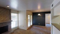 This single-story space showcases an open-concept living and dining area that feels bright and airy, thanks to multiple windows fitted with horizontal blinds and a set of glass-paned French doors that invite natural light throughout the day. The living area features wall-to-wall carpet in a neutral tan tone, providing a warm and comfortable foundation underfoot.

A standout architectural detail is the bold, deep navy accent wall in the dining area, which creates a striking contrast against the surrounding neutral white walls. A classic pendant light hangs above this space, adding a focal point and functional overhead lighting to the dining zone. The textured popcorn ceiling adds a layer of visual depth while maintaining a traditional aesthetic throughout.

The open layout allows the living and dining areas to flow seamlessly into one another, with a doorway visible leading to additional rooms beyond. The combination of ample natural light, neutral tones, and the dramatic accent wall creates a balanced ambiance that is both functional and visually interesting, making this a versatile and welcoming living space.