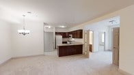 This single-floor residence offers an open-concept design that seamlessly connects the kitchen and living areas, creating a spacious and functional flow throughout. The kitchen serves as the focal point of the main living space, featuring rich dark wood cabinetry that provides ample storage, light-toned countertops, and a peninsula with an integrated sink — ideal for both meal preparation and casual dining. Stainless steel appliances, including a built-in microwave and range, complement the space alongside a full-size white refrigerator. The kitchen opens directly into the generously sized living area, which is finished with plush, light-colored carpeting that adds warmth and comfort underfoot. Neutral cream-toned walls and flush-mount lighting maintain a clean, bright ambiance throughout. A private entry door with a classic panel design is visible from the main living area, offering convenient access. Adjacent rooms, accessible through interior doorways, appear to include a bedroom and a bathroom with natural light filtering in, suggesting a well-distributed floor plan. Overall, the space presents a cohesive, move-in-ready interior with a balanced combination of practical features and comfortable living spaces.