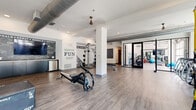 Located at 11325 Park Vista Blvd in Fort Worth, TX, this generously sized fitness center offers a well-appointed, single-floor layout designed to accommodate a comprehensive workout experience. The space is divided into distinct functional zones, seamlessly connected through black-framed glass doors that lend a modern, industrial aesthetic throughout.

The main workout floor features durable wood-look flooring and white walls accented with bold motivational typography and graphics, creating an energetic and encouraging atmosphere. Exposed silver ductwork runs along the ceilings, complementing the contemporary industrial design, while ceiling fans and recessed lighting ensure comfort throughout.

The cardio zone is bathed in natural light from expansive floor-to-ceiling windows with black steel frames, offering outdoor views and an open, airy feel. Matrix-brand stationary bikes, ellipticals, and treadmills are neatly arranged in this well-lit area. A dedicated strength training zone houses a multi-functional cable machine, adjustable benches, free weights, and additional resistance equipment. A separate spin studio with colorful exercise balls adds variety to the offerings.

Dark cabinetry along one wall provides storage, and a small refrigerator unit is conveniently accessible. The overall design balances functionality with an inviting, motivating ambiance suited for a wide range of fitness routines.