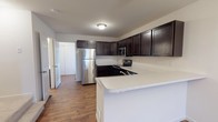 This three-floor home at 3503 is designed with a practical and modern aesthetic throughout. The main living level showcases warm wood-look flooring that extends across an open-concept layout, connecting the living area to the kitchen. A chandelier anchors the living space, adding a touch of elegance to the open floor plan.

The kitchen is a standout feature, equipped with rich dark cabinetry offering ample storage, light-toned countertops, and a full suite of stainless steel appliances including a refrigerator, electric range, microwave, and dishwasher. A peninsula provides additional counter space and creates a natural division between the kitchen and living area.

The bedrooms are carpeted for comfort and include ceiling fans with light fixtures. The primary bedroom benefits from an en-suite bathroom featuring dark cabinetry and a walk-in closet, while additional bedrooms offer natural light through windows. Bathrooms are finished with chrome fixtures, including a standalone shower with sliding glass doors.

The lowest level features an unfinished basement with concrete walls and exposed joists, offering significant potential for customization or additional storage.