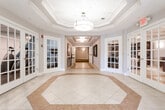 Located at 140 Mayhill St in Saddle Brook, New Jersey, this residential building offers thoughtfully designed common areas that combine functionality with refined aesthetics. The main entry lobby features an impressive octagonal tray ceiling with a statement pendant light fixture, complemented by large light-filled windows and glass-paned French doors that open to adjoining spaces, including what appears to be a dining area and lounge. The flooring showcases an elegant two-tone tile pattern with a geometric inlay, creating a polished and welcoming first impression.

A connected corridor leads deeper into the building, highlighted by a coffered ceiling with recessed flush-mount lighting and decorative wall art, transitioning from tile to carpeted flooring as it extends through the interior hallways. The elevator lobby features three stainless steel elevator doors set against wainscoted walls, providing convenient multi-floor access. Nearby, a dedicated mailroom houses a full bank of individual mailboxes alongside a resident information bulletin board.

The building's carpeted residential corridors are finished with crown molding, wainscoting, and wall sconce lighting, creating a warm and navigable pathway to individual units. Directional signage assists residents in locating specific unit ranges. Overall, the common areas reflect a clean, classic design sensibility with consistent neutral tones throughout.