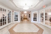 Located at 140 Mayhill St in Saddle Brook, New Jersey, this residential building offers thoughtfully designed common areas that combine functionality with refined aesthetics. The main entry lobby features an impressive octagonal tray ceiling with a statement pendant light fixture, complemented by large light-filled windows and glass-paned French doors that open to adjoining spaces, including what appears to be a dining area and lounge. The flooring showcases an elegant two-tone tile pattern with a geometric inlay, creating a polished and welcoming first impression.

A connected corridor leads deeper into the building, highlighted by a coffered ceiling with recessed flush-mount lighting and decorative wall art, transitioning from tile to carpeted flooring as it extends through the interior hallways. The elevator lobby features three stainless steel elevator doors set against wainscoted walls, providing convenient multi-floor access. Nearby, a dedicated mailroom houses a full bank of individual mailboxes alongside a resident information bulletin board.

The building's carpeted residential corridors are finished with crown molding, wainscoting, and wall sconce lighting, creating a warm and navigable pathway to individual units. Directional signage assists residents in locating specific unit ranges. Overall, the common areas reflect a clean, classic design sensibility with consistent neutral tones throughout.