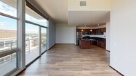 This modern, single-floor unit is designed to maximize natural light and panoramic views through expansive floor-to-ceiling windows that span multiple rooms. The open living area features smooth hardwood flooring and direct access to a balcony, framing lush treetop and urban skyline vistas. The well-appointed kitchen is outfitted with rich dark-stained wood cabinetry, dark granite countertops, a full suite of stainless steel appliances including a refrigerator, dishwasher, and range, and a peninsula with pendant lighting that creates a natural divide between kitchen and living spaces. Bedrooms are carpeted for comfort and benefit from generous window coverage, offering sweeping views of the surrounding greenery, waterway, and cityscape. The bathroom includes a vanity with dark granite countertops, dark wood cabinetry, and accessibility features such as a grab bar near the toilet. A dedicated in-unit laundry area with a stacked washer and dryer adds everyday convenience. Throughout the unit, dark-framed interior doors, modern wall sconces, and neutral wall tones contribute to a cohesive, contemporary aesthetic. The elevated position of the unit enhances the sense of openness and provides striking views in multiple directions.