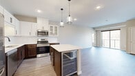 Located at 6470 37th Ave NW in Rochester, MN, this thoughtfully designed one-bedroom, two-bathroom residence offers a highly functional single-floor layout with modern finishes throughout. The open-concept kitchen is a standout feature, equipped with stainless steel appliances, crisp white upper cabinetry, warm wood-toned lower cabinets, a subway tile backsplash, and a central island with a quartz countertop, built-in beverage cooler, and bar seating — all illuminated by stylish pendant lighting. The kitchen flows seamlessly into the living room, where light-toned hardwood floors, neutral walls, and a large sliding glass door create a bright, welcoming atmosphere with outdoor views. The primary bedroom is a comfortable retreat, featuring plush carpet, large windows overlooking a green landscape, and direct access to a spacious walk-in closet with wire shelving on three walls. The two bathrooms are finished with warm wood vanities, white countertops, and clean, contemporary fixtures. Recessed lighting and a consistent neutral color palette unify the space, lending it a polished, modern aesthetic well-suited for everyday living.