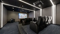 Located at 50 Morgan Street in Hartford, Connecticut, this dedicated screening room delivers a true cinematic experience within a thoughtfully designed, single-level space. The room is anchored by a large, wall-mounted projection screen at the front, paired with a ceiling-mounted projector that ensures a crisp, immersive viewing experience. Rows of premium black leather power recliners with built-in cup holders are arranged across two tiered levels, providing unobstructed sightlines from every seat. The dark, drop-panel ceiling is outfitted with recessed lighting and sleek linear LED light strips that run along the perimeter, creating a dramatic, atmosphere-enhancing ambiance. Vertical LED accent panels on the side walls add a modern, polished touch to the room's overall aesthetic. The floors are covered in deep blue-gray commercial carpeting that complements the room's dark, sophisticated color palette of charcoal, slate, and black throughout. A beverage storage unit is positioned along one side wall for added convenience. The space is accessed through a clearly marked exit door, and the acoustically treated, textured wall panels contribute to an optimized audio environment. This screening room is well-suited for private film screenings, entertainment events, or group viewings.