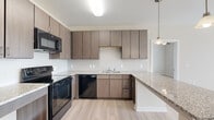 Located at 1140 Bridgefield Pl in Charlotte, NC, this single-floor residence offers a thoughtfully designed layout with 2 bedrooms and 2 bathrooms. The open-concept kitchen is a standout feature, showcasing contemporary taupe cabinetry, granite-look countertops, a peninsula breakfast bar with pendant lighting, and black appliances including a range, microwave, and dishwasher. Light wood-tone luxury vinyl plank flooring runs throughout the main living areas, creating a clean and cohesive aesthetic. The spacious living room is filled with natural light from large windows and a glass-panel door, complemented by a ceiling fan overhead. A connecting hallway leads to both bedrooms and includes a dedicated closet for additional storage. Each bedroom features plush carpeting, a ceiling fan, and windows with blinds that allow ample natural light. The generously sized primary bedroom offers a comfortable retreat. Both bathrooms are finished with wood-tone cabinetry, granite-style countertops, and luxury vinyl plank flooring, with tub-shower combinations. The overall ambiance is modern, clean, and move-in ready, offering a functional and comfortable living environment.