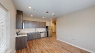 This single-story 2-bedroom, 2-bathroom unit in Baton Rouge, Louisiana offers a clean, modern aesthetic throughout. The open kitchen is a standout feature, showcasing dark gray cabinetry with brushed nickel hardware, white quartz-style countertops, and a full suite of stainless steel appliances including a range, over-the-range microwave, dishwasher, and refrigerator. Warm wood-look vinyl plank flooring flows consistently through the main living areas and bedrooms, adding both durability and visual cohesion. Recessed lighting throughout provides a bright, well-lit environment. Both bedrooms are comfortably sized, each featuring a ceiling fan, a window with blinds that invites natural light and outdoor views, and a closet with built-in shelving. The two bathrooms are finished with neutral tile flooring, and each includes a tub/shower combo with shelving. One bathroom features a dark wood vanity with a light countertop and a mirror, adding a touch of refinement. The layout, as seen in the dollhouse view, is efficiently arranged with a practical hallway connecting the living areas to the private bedrooms, making this a functional and attractive unit.