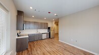 This single-story 2-bedroom, 2-bathroom unit in Baton Rouge, Louisiana offers a clean, modern aesthetic throughout. The open kitchen is a standout feature, showcasing dark gray cabinetry with brushed nickel hardware, white quartz-style countertops, and a full suite of stainless steel appliances including a range, over-the-range microwave, dishwasher, and refrigerator. Warm wood-look vinyl plank flooring flows consistently through the main living areas and bedrooms, adding both durability and visual cohesion. Recessed lighting throughout provides a bright, well-lit environment. Both bedrooms are comfortably sized, each featuring a ceiling fan, a window with blinds that invites natural light and outdoor views, and a closet with built-in shelving. The two bathrooms are finished with neutral tile flooring, and each includes a tub/shower combo with shelving. One bathroom features a dark wood vanity with a light countertop and a mirror, adding a touch of refinement. The layout, as seen in the dollhouse view, is efficiently arranged with a practical hallway connecting the living areas to the private bedrooms, making this a functional and attractive unit.