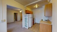 Located at 600 James St in Syracuse, NY, this single-floor studio offers a blend of classic architectural character and functional living. The main living area is generously proportioned, featuring wall-to-wall carpet, crown molding, decorative panel framing along the walls, and a ceiling fan with integrated lighting. Multiple windows dressed with curtains allow natural light to fill the space, and a radiator provides in-unit heating. A closet and additional doorways provide practical storage and connectivity throughout the unit. The kitchen is efficiently laid out with warm wood cabinetry, a gas range, a full-size refrigerator, a countertop sink, and tile flooring, transitioning seamlessly from the carpeted living space. A charming white-framed glass-panel door connects the kitchen to the living area, adding a touch of vintage character. The bathroom features a wood-framed vanity with a built-in medicine cabinet and mirror, mosaic tile flooring, and a classic solid wood door with original hardware. Throughout the unit, details such as crown molding, panel molding accents, and ceiling fans reflect the building's traditional architectural roots, creating a space with character and practicality.