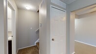This three-floor residence offers a practical and well-organized layout across its multiple levels. The kitchen is designed in a galley style, featuring dark espresso cabinetry that extends from floor to ceiling on both sides, light laminate countertops, and a full suite of stainless steel and black appliances including a refrigerator, range, and over-the-range microwave. The living areas are finished with wall-to-wall carpeting in neutral tones, complemented by warm beige walls throughout. Large windows dressed with vertical blinds allow natural light to fill the main living and bedroom spaces, offering pleasant outdoor views. A full bathroom on the upper level includes a tub-shower combination with a curved curtain rod, a dark-cabineted vanity with a light countertop, and tile-effect flooring. A half bathroom provides a vanity and toilet with matching finishes. Carpeted stairways with white railings connect the floors, and textured ceilings are consistent throughout the upper levels. The lower level includes a finished room with drop-ceiling tiles and recessed lighting, ideal for a recreation or bonus room, as well as an unfinished utility and storage area with exposed joists and concrete flooring, offering generous potential for customization.