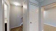 This three-floor residence offers a practical and well-organized layout across its multiple levels. The kitchen is designed in a galley style, featuring dark espresso cabinetry that extends from floor to ceiling on both sides, light laminate countertops, and a full suite of stainless steel and black appliances including a refrigerator, range, and over-the-range microwave. The living areas are finished with wall-to-wall carpeting in neutral tones, complemented by warm beige walls throughout. Large windows dressed with vertical blinds allow natural light to fill the main living and bedroom spaces, offering pleasant outdoor views. A full bathroom on the upper level includes a tub-shower combination with a curved curtain rod, a dark-cabineted vanity with a light countertop, and tile-effect flooring. A half bathroom provides a vanity and toilet with matching finishes. Carpeted stairways with white railings connect the floors, and textured ceilings are consistent throughout the upper levels. The lower level includes a finished room with drop-ceiling tiles and recessed lighting, ideal for a recreation or bonus room, as well as an unfinished utility and storage area with exposed joists and concrete flooring, offering generous potential for customization.