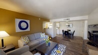 This single-floor residence offers a thoughtfully designed layout that balances comfort and functionality across its key living spaces. The open-plan living and dining area serves as the heart of the home, featuring durable wood-style flooring, a warm gold accent wall, and a sliding glass door that invites natural light and provides access to an outdoor patio with surrounding greenery. The adjoining dining area is illuminated by a pendant light fixture, creating a welcoming atmosphere for meals and gatherings. The galley-style kitchen is efficiently arranged with white cabinetry, light countertops, a gas range, dishwasher, refrigerator, and a built-in microwave. Track lighting brightens the workspace, and a dedicated walk-in pantry offers generous storage. Two well-proportioned bedrooms feature plush carpeting, natural window light, and ample closet space. The primary bedroom includes a ceiling fan and access to a walk-in closet. Both bathrooms are finished with light countertops, white cabinetry, and wood-style flooring — one featuring a full tub-shower combination with a well-lit vanity mirror. Completing the unit is a dedicated laundry room equipped with a full-size washer and dryer beneath generous upper cabinetry storage.