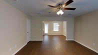 This two-story property offers a well-designed layout that balances open, connected living spaces with practical functionality. The main living area features rich, dark hardwood flooring that extends seamlessly into an adjoining dining or flex space, creating a sense of continuity and flow throughout the lower level. Neutral beige walls provide a warm, versatile backdrop that complements a variety of furnishing styles. A ceiling fan with integrated lighting fixture serves as a central overhead element, enhancing air circulation and ambient light throughout the space. Textured ceilings add a subtle tactile dimension to the interior. Natural light filters in through windows near the entryway, brightening the space and highlighting the clean white trim and baseboards that frame each room. A side door with a sidelite window provides additional light and easy access. The open archway between the main living area and the adjoining space encourages an airy, connected feel. A thermostat panel is conveniently positioned on the wall, reflecting thoughtful placement of home systems. The overall ambiance is clean, neutral, and move-in ready, offering a solid foundation for personalization across both floors of the home.