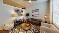 Located at 4701 Forest Dr in Forest Acres, SC, this single-floor residence blends contemporary design with warm, eclectic touches throughout. A welcoming hallway sets the tone immediately, featuring rich hardwood flooring, crisp white walls, and a striking sliding barn door with matte black hardware. A round wall mirror adds a decorative accent, while the open sightline draws the eye toward the kitchen beyond.

The kitchen is a standout space, equipped with gray shaker-style cabinetry, stainless steel appliances, a subway tile backsplash, and a large center island topped with light stone countertops. Pendant lighting in matte black hangs above the island, complementing gold-toned fixtures at the sink. Large vertical blinds allow abundant natural light to filter in, brightening the hardwood floors throughout.

The living area offers a comfortable, curated atmosphere with a ceiling fan, bold geometric area rug, and room for stylish furnishings. The bedroom features a vibrant burnt orange accent wall, plush carpeting, and access to a dedicated walk-in closet. The bathroom is finished with wood-look tile flooring, a subway-tiled tub surround, and a granite-topped vanity with gray cabinetry, offering a clean and functional design.