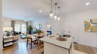 Located at 120 Lullwater Dr in Evans, Georgia, this single-floor residence offers a thoughtfully designed open-concept layout that seamlessly connects the kitchen, dining, and living areas. The kitchen is a standout feature, showcasing crisp white shaker cabinetry, granite countertops, a central island with a built-in sink and pendant lighting overhead, and a full suite of stainless steel appliances including a range, microwave, and refrigerator. Light wood-style flooring flows throughout the main living areas, enhancing the bright, airy atmosphere. The living room is generously sized, anchored by a ceiling fan and French doors that open to an outdoor balcony, inviting natural light and outdoor views. The dining area sits comfortably between the kitchen and living room, ideal for everyday meals or entertaining. The primary bedroom is a serene retreat featuring plush carpeting and a well-appointed en-suite bathroom with granite vanity countertops, white cabinetry, and a walk-in closet. A second bedroom also includes carpeted flooring and its own walk-in closet. Throughout the residence, neutral tones and recessed lighting create a cohesive, welcoming ambiance suited to a variety of living styles.