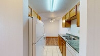 This one-bedroom, two-bathroom unit in Fargo, North Dakota offers a well-organized, single-floor layout designed for comfortable everyday living. The galley-style kitchen is efficiently arranged with warm oak cabinetry lining both sides, green-toned countertops, tile flooring, and a full suite of white appliances including a refrigerator, electric range, built-in microwave, and dishwasher. A ceiling fan and overhead fluorescent lighting keep the space bright and functional. The kitchen opens directly into the living area, which features neutral carpet, baseboard heating, and a sliding glass door that leads to a private balcony with outdoor views. The bedroom is a comfortable size with soft carpet, a mirrored sliding closet, and a window that brings in natural light. Three closets throughout the unit provide generous storage. Both bathrooms are finished with tile flooring and oak vanities; one includes a tub-shower combination with white tile surround, while the other is a three-quarter bath. Textured ceilings and warm wood trim are consistent throughout, giving the unit a cohesive, classic feel. The overall layout is practical and makes efficient use of every square foot.