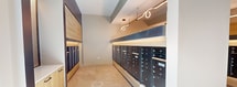 This contemporary mail center, located at 14100 John Henry Faulk Dr in Pflugerville, TX, offers a well-designed space for efficient mail management. The 1080 square foot single-floor layout is characterized by its clean lines and functional design. Upon entering, residents are greeted by an expansive area with high ceilings, creating an open and airy atmosphere.

The space is dominated by two parallel rows of sleek, dark-colored mailboxes, providing ample individual units for the building's occupants. Above these mailbox arrays, innovative curved lighting fixtures add a touch of modern elegance while ensuring excellent visibility. The center's design incorporates small windows near the ceiling, allowing natural light to complement the artificial lighting.

Neutral-toned tile flooring extends throughout, offering durability and easy maintenance. The walls are painted in a light, calming color, contributing to the space's bright and welcoming ambiance. Strategic placement of support columns maintains the open feel while providing structural integrity.

Near the entrance, a glass door allows visibility to the outside, creating a connection with the surrounding environment. The layout is intuitively designed for easy navigation, with clear pathways between mailbox sections and towards the exit. This thoughtful arrangement ensures a smooth flow of traffic, even during peak usage times.

Overall, this mail center combines functionality with contemporary aesthetics, providing residents with a pleasant and efficient space for their postal needs.