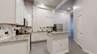 Located at 101 N Kansas Ave in downtown Topeka, KS, this three-bedroom, one-bathroom unit combines modern finishes with industrial character across a single, well-organized floor. The kitchen serves as a standout centerpiece, featuring crisp white shaker cabinetry, granite countertops, a tile backsplash with decorative accents, stainless steel appliances, and a central island with pendant lighting suspended from above. Exposed ductwork and wooden ceiling beams add an urban loft aesthetic that carries throughout the space. The generously sized primary bedroom offers ample room and connects to a walk-in closet outfitted with built-in shelving and a full hanging rod. The two additional bedrooms are well-proportioned with patterned carpet flooring, high ceilings, and neutral walls that create a clean, versatile backdrop. One bedroom benefits from dual windows that bring in natural light and views of the surrounding area. The shared bathroom features a double-sink vanity with granite countertops, white cabinetry, wall-mounted sconces, a large mirror, and tile flooring, offering a refined and functional space. Throughout the unit, tile and carpet flooring, high ceilings, and a neutral color palette contribute to a cohesive, modern ambiance.
