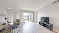 This single-floor unit offers a thoughtfully designed layout with a bright, neutral palette and light wood-style flooring that flows consistently throughout the space. The living room is generously proportioned, featuring textured ceilings with crown molding, large sliding glass doors that open onto a private balcony, and vertical blinds that diffuse natural light evenly across the room. The balcony provides open views of the surrounding neighborhood, adding an airy quality to the living area.

The galley-style kitchen is well-appointed with gray cabinetry, granite-look countertops, white subway tile backsplash, and a full suite of stainless steel appliances, including a refrigerator, dishwasher, and range. Track lighting above keeps the space bright and functional.

The bedroom is comfortably sized with soft gray walls, a ceiling fan, textured ceiling, and its own sliding glass door leading directly to the balcony—filling the room with natural light and outdoor access. The bathroom maintains the unit's clean aesthetic with a granite-topped vanity, tiled tub-shower combination, and wood-style flooring. Overall, the unit presents a cohesive, modern feel with practical finishes throughout.