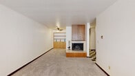Located at 2570 N Maryland Ave in Milwaukee's vibrant East Side neighborhood, this one-bedroom, one-bathroom residence offers a well-organized and functional layout across a single floor. The living room serves as the centerpiece of the home, highlighted by a wood-paneled fireplace with a raised hearth and built-in shelving and cabinetry along the adjacent wall. A ceiling fan overhead and soft carpeting underfoot contribute to the room's comfortable, lived-in feel. The kitchen area connects seamlessly via a hallway featuring a striking blue-and-white checkered tile floor, warm wood-trimmed doorframes, louvered closet doors, and wood cabinetry with ample overhead storage. The bedroom is a quiet, carpeted retreat with a large window fitted with horizontal blinds, a wood sill, and baseboard heating, allowing for natural light and year-round comfort. The bathroom is clean and straightforward, offering a full tiled tub-and-shower combination, a toilet, and a mirrored medicine cabinet. A dedicated closet provides additional storage. The overall aesthetic blends mid-century practicality with warm wood accents and neutral tones, creating a cohesive and inviting living environment.