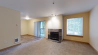 This single-floor residence offers a thoughtfully designed layout with a warm, neutral color palette throughout. The spacious living room serves as the heart of the home, anchored by a striking tile-surround fireplace and track lighting that highlights the feature wall. Plush carpeting adds comfort underfoot, while sliding glass doors open to a private balcony overlooking lush greenery, and a large window with blinds allows abundant natural light to fill the room. The kitchen is efficiently designed with light maple cabinetry, dark laminate countertops, a double stainless steel sink, and stainless steel appliances including a refrigerator, microwave, dishwasher, and range. A breakfast bar provides a convenient casual dining option, and wood-look flooring extends throughout the kitchen area. A hallway connects the living spaces to the private quarters, where the bedrooms feature plush carpeting, soft natural light from windows with views of surrounding trees, and generous closet space with sliding panel doors. The bathroom includes a full tub-shower combination. The overall ambiance is clean, comfortable, and move-in ready, with consistent warm tones and practical finishes throughout.