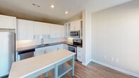 Located at 125 Remount Rd in Charlotte's vibrant 28203 zip code, this single-floor residence offers a well-designed layout with modern finishes throughout. The kitchen is a standout feature, boasting crisp white shaker cabinetry — including glass-front upper cabinets — a stainless steel appliance suite with a French door refrigerator, electric range, microwave, and dishwasher. A light-toned countertop island provides additional prep and dining space, while a classic subway tile backsplash adds a clean, contemporary touch. Rich hardwood-style flooring flows seamlessly through the kitchen and into the adjacent living and dining area, which is bathed in natural light through large windows and a set of French doors. A ceiling fan adds comfort to the bright, open living space. The walk-in closet is outfitted with multi-tier wire shelving and carpeted flooring, offering generous, well-organized storage. The full bathroom features white cabinetry, a dark granite-style countertop, a framed mirror, and a tiled tub-shower combination with warm beige tile surround. Neutral wall tones throughout create a cohesive, move-in-ready atmosphere well-suited for comfortable everyday living.