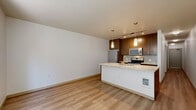 Located at 4745 40th Ave SW in Seattle's West Seattle neighborhood, this one-bedroom, one-bathroom unit is thoughtfully laid out across a single floor, making efficient use of its compact footprint. Light wood-style flooring runs throughout the space, lending a warm, cohesive aesthetic from room to room.

The open-concept living and kitchen area serves as the heart of the unit. The kitchen is equipped with stainless steel appliances—including a refrigerator, microwave, and range—and features rich wood cabinetry, a stone-topped peninsula with pendant lighting overhead, and a tile backsplash. Track lighting adds functional illumination to the cooking space, while the adjoining living area offers a clean, open canvas with neutral walls.

The bedroom is a cozy, well-proportioned room with a ceiling fan, smooth white walls, and access to a closet. A hallway connects the main living areas to the private spaces and includes additional storage. The bathroom is finished with a stone-top vanity, warm wood cabinetry, a large mirror, and a walk-in shower, maintaining the modern and clean design language found throughout the unit. The overall ambiance is contemporary, neutral, and move-in ready.