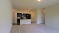 Located at 130 Ocean Aisle Circle in Salisbury, Maryland, this single-floor residence offers a well-designed open-concept layout that seamlessly connects the living and kitchen areas. The spacious living area is finished with plush, light-toned carpeting that adds warmth and comfort underfoot, while the clean, neutral wall colors create a bright and welcoming atmosphere throughout.

The kitchen is a standout feature, showcasing dark espresso cabinetry that provides a striking contrast against the lighter surroundings. A central island with a sink serves as both a functional workspace and a casual gathering point, illuminated by stylish pendant lights that hang overhead. Recessed lighting further enhances the kitchen's brightness. Black appliances, including a refrigerator, microwave, and range, complement the dark cabinetry, while the countertops offer ample prep space. The kitchen floor transitions to hard surface flooring, distinguishing it from the carpeted living area.

Multiple doorways visible from the main living space suggest easy access to additional rooms and storage areas, including what appears to be a closet with double doors. The overall layout is practical and inviting, offering a clean, move-in-ready environment suited for comfortable everyday living in Salisbury, MD.