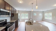 This single-floor residence offers a thoughtfully designed open-concept layout that seamlessly connects the kitchen, dining, and living areas. The kitchen is well-appointed with dark espresso cabinetry extending to the ceiling for ample storage, stainless steel appliances including a refrigerator with ice maker, electric range, and microwave. A central island with granite countertops and an undermount sink serves as a functional focal point, illuminated by stylish pendant lights overhead. Recessed lighting and neutral gray walls complement the warm hardwood-style flooring that flows throughout the main living spaces.

The living area is generously proportioned, featuring multiple windows that invite abundant natural light and outdoor views of surrounding greenery. White panel doors lead to closets and additional rooms, maintaining a clean, cohesive aesthetic. The bedroom is carpeted and bright, with a large window offering neighborhood views. The bathroom features matching dark cabinetry with granite countertops, an undermount sink, hardwood-style flooring, and accessibility grab bars. Throughout the unit, white trim and neutral tones create a modern, move-in-ready atmosphere.