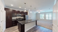 This single-floor residence is designed with an open-concept layout that seamlessly connects the kitchen and living area, creating a cohesive and functional living space. The kitchen is a standout feature, showcasing rich dark-espresso cabinetry that extends to the ceiling, complemented by dark granite countertops and a full suite of stainless steel appliances, including a refrigerator, range, and microwave. A large central island with a built-in sink, pendant lighting overhead, and a wine rack below serves as both a practical workspace and a visual focal point. Recessed lighting and crown molding add a polished, finished quality to the kitchen and adjoining living area.

The living space transitions smoothly from hardwood-style flooring in the kitchen to plush carpet, and features a ceiling fan and natural light from windows with outdoor views. The bedrooms are carpeted and generously sized, each equipped with a ceiling fan. The primary bedroom includes access to a walk-in closet and an en-suite bathroom. The bathroom features a tub and shower combination with brushed nickel fixtures, tile flooring, and granite countertops, maintaining the consistent design language found throughout the space.