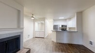 This single-story residence offers a thoughtfully arranged floor plan that makes efficient use of its space. The open-concept living and kitchen area serves as the heart of the home, where wood-style flooring runs throughout and connects the two spaces seamlessly. The kitchen features crisp white shaker cabinets, a peninsula with a light grey countertop that doubles as a breakfast bar, and a full suite of stainless steel appliances including a refrigerator, range, and microwave. A ceiling fan in the living area adds both comfort and style, while a fireplace provides a cozy focal point. Sliding glass doors with vertical blinds open to an outdoor patio area, bringing in natural light and offering outdoor access. The bedroom is a comfortable retreat with plush carpeting, a natural light window with baseboard heating below, and direct access to a closet that also houses in-unit washer and dryer connections. Neutral wall tones throughout create a clean, move-in-ready ambiance. A textured ceiling and recessed lighting complete the overall look, lending the space a polished, functional character suited for everyday living.
