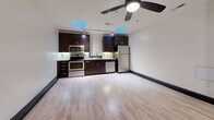 This studio unit at 50 W Fourth St, Apt. 215 in Winston-Salem, NC offers a well-designed open-concept layout that efficiently combines the living and kitchen areas. The kitchen is equipped with stainless steel appliances — including a range, microwave, dishwasher, and refrigerator — paired with rich dark cabinetry, granite-style countertops, and under-cabinet lighting. Light hardwood flooring runs throughout, complemented by bold dark baseboards. Skylights and a ceiling fan enhance the bright, airy feel. The bathroom includes a full soaking tub/shower combo with clean white surroundings.