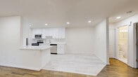 Located at 19 Vermeer Drive in South Amboy, NJ, this 2-bedroom, 1-bathroom unit offers a clean, modern interior with a well-organized layout. Entry is via a classic staircase with white-painted risers, warm wood treads, and a dark handrail, leading up to the main living level. The open-plan kitchen and dining area is a standout feature, boasting bright white shaker-style cabinetry, white quartz countertops, a subway tile backsplash, and stainless steel appliances including a refrigerator, range, microwave, and dishwasher. Light-toned tile flooring completes the contemporary look of this space. The living room features gleaming hardwood floors, recessed lighting, and a wide window with outdoor greenery views, filling the room with natural light. Both bedrooms continue the hardwood flooring theme, with the primary bedroom offering generous proportions, a window with garden views, and a wall-unit air conditioner alongside baseboard heating. The second bedroom is similarly bright and well-proportioned. The bathroom features a clean white tiled tub-shower surround and white vanity cabinetry. Two closets and a hallway add practical storage and circulation throughout this efficiently designed home.
