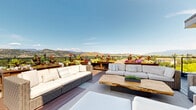 Located at 235 Hollywood Rd N in Kelowna, British Columbia, this impressive rooftop terrace offers a exceptional outdoor living experience set against the breathtaking backdrop of the Okanagan Valley's rolling mountains and open skies. The deck is finished with composite wood decking in contrasting tones and is divided into several distinct zones designed for relaxation and socializing.

One area features a sophisticated lounge arrangement with wicker and upholstered sectional sofas, complemented by a striking live-edge wood coffee table and built-in planter boxes overflowing with vibrant seasonal flowers. A second, more casual area is outfitted with colorful Adirondack chairs and small side tables, perfect for taking in the unobstructed panoramic views behind a sleek railing system. A timber pergola adds architectural character and partial shade to a transitional gathering zone near large glass sliding doors that connect to an indoor space.

Brick and panel exterior cladding lend the structure a solid, refined aesthetic. The rooftop's generous footprint accommodates multiple seating configurations simultaneously, making it well-suited for both intimate gatherings and larger events. Abundant natural light floods the space throughout the day, and the elevated position above the Kelowna cityscape ensures remarkable, uninterrupted views from every angle.