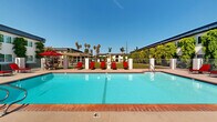 Located at 10800 Pioneer Blvd in Santa Fe Springs, California, this well-maintained residential community offers a welcoming environment defined by its thoughtfully landscaped grounds and an array of shared amenities. The multi-building complex features stucco exteriors finished in crisp white, accented by lush climbing vines that add a distinctive, verdant character to each building facade. Arched entryways, upper-level balconies, and exterior stairwells contribute to the architectural charm throughout the property.

The expansive outdoor common areas are a true highlight of the community. A generously sized swimming pool, framed by brick coping and a wide pool deck, is appointed with red lounge chairs and shaded seating areas, making it an inviting spot for relaxation. Tall palm trees and mature greenery surround the pool area, enhancing the sense of a private retreat.

Residents also enjoy a dedicated playground equipped with a multi-level play structure, set against a backdrop of open green lawn — ideal for outdoor recreation. A pergola-covered seating area nearby provides a comfortable gathering space. Wide concrete walkways connect the buildings across well-kept lawns and manicured shrubbery, creating an accessible and pleasant pedestrian experience throughout the community.