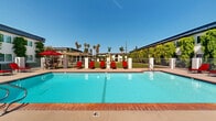Located at 10800 Pioneer Blvd in Santa Fe Springs, California, this well-maintained residential community offers a welcoming environment defined by its thoughtfully landscaped grounds and an array of shared amenities. The multi-building complex features stucco exteriors finished in crisp white, accented by lush climbing vines that add a distinctive, verdant character to each building facade. Arched entryways, upper-level balconies, and exterior stairwells contribute to the architectural charm throughout the property.

The expansive outdoor common areas are a true highlight of the community. A generously sized swimming pool, framed by brick coping and a wide pool deck, is appointed with red lounge chairs and shaded seating areas, making it an inviting spot for relaxation. Tall palm trees and mature greenery surround the pool area, enhancing the sense of a private retreat.

Residents also enjoy a dedicated playground equipped with a multi-level play structure, set against a backdrop of open green lawn — ideal for outdoor recreation. A pergola-covered seating area nearby provides a comfortable gathering space. Wide concrete walkways connect the buildings across well-kept lawns and manicured shrubbery, creating an accessible and pleasant pedestrian experience throughout the community.