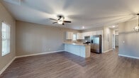 This single-story home presents a cohesive, modern design unified by warm wood-look flooring and neutral taupe walls throughout. The open-concept living and kitchen area forms the heart of the home, where a ceiling fan with light fixture anchors the generous living space. Natural light filters in through multiple windows fitted with white blinds, creating a bright and welcoming atmosphere.

The kitchen is well-appointed with crisp white cabinetry extending to the ceiling, light granite-style countertops, a peninsula that defines the space, and a full suite of stainless steel appliances including a French door refrigerator, electric range, and dishwasher. A window above the sink adds additional natural light.

The bedrooms are comfortably sized, each featuring wood-look flooring, neutral walls, and windows with outdoor views. The primary bedroom includes a ceiling fan and direct access to a private bathroom. The bathrooms are consistently finished with white vanity cabinetry, granite-style countertops, and wood-look flooring. A dedicated laundry room includes wire shelving overhead and plumbing and electrical connections for a washer and dryer.