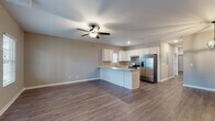 This single-story home presents a cohesive, modern design unified by warm wood-look flooring and neutral taupe walls throughout. The open-concept living and kitchen area forms the heart of the home, where a ceiling fan with light fixture anchors the generous living space. Natural light filters in through multiple windows fitted with white blinds, creating a bright and welcoming atmosphere.

The kitchen is well-appointed with crisp white cabinetry extending to the ceiling, light granite-style countertops, a peninsula that defines the space, and a full suite of stainless steel appliances including a French door refrigerator, electric range, and dishwasher. A window above the sink adds additional natural light.

The bedrooms are comfortably sized, each featuring wood-look flooring, neutral walls, and windows with outdoor views. The primary bedroom includes a ceiling fan and direct access to a private bathroom. The bathrooms are consistently finished with white vanity cabinetry, granite-style countertops, and wood-look flooring. A dedicated laundry room includes wire shelving overhead and plumbing and electrical connections for a washer and dryer.