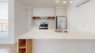 Located at 9675 Avenue Papineau in Montréal, this well-designed one-bedroom, one-bathroom unit offers a clean, modern aesthetic throughout. Light-toned hardwood flooring flows consistently across the entire space, complementing the bright white walls and creating a cohesive, airy atmosphere.

The open-concept kitchen and living area serves as the heart of the unit. The kitchen is outfitted with white flat-front cabinetry, warm wood open shelving accents, a marble-style backsplash, stainless steel appliances, and a large waterfall-edge island with pendant globe lighting — ideal for both cooking and entertaining. The adjacent living area benefits from an impressive wall of floor-to-ceiling windows and a glass-railed balcony door, flooding the space with natural light and offering views of the surrounding Montréal neighbourhood.

The bedroom is a comfortable, well-proportioned room featuring a tall window with neighbourhood views, light hardwood flooring, and a sliding-door closet with built-in shelving for organized storage.

The bathroom is finished to a modern standard, featuring large-format neutral tiles, a sleek frameless sliding glass shower enclosure, a wall-mounted vanity with an undermount sink, and clean, minimal fixtures throughout.

A hallway connects all rooms efficiently, maintaining a logical and practical layout that maximizes the use of the available space.