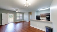 This single-floor residence at 451 Johns Rd NW in Huntsville, Alabama offers a well-designed open-concept layout with a cohesive, light-toned interior throughout. The living area is bright and spacious, featuring rich hardwood flooring and a ceiling fan paired with an elegant chandelier. Large windows and a glass-paneled door provide natural light and direct access to a private balcony overlooking lush greenery.

The kitchen is efficiently designed in a galley style, outfitted with dark espresso cabinetry, granite-style countertops, black appliances including a refrigerator and range with over-the-range microwave, and a stainless steel sink. A raised breakfast bar peninsula connects the kitchen to the living space, making it ideal for casual dining or entertaining.

The bedrooms are carpeted for comfort, each equipped with ceiling fans and ample closet space. One bedroom features dual windows that invite generous natural light and outdoor views, while another includes multiple doorways suggesting access to a closet and additional spaces.

The bathroom is clean and functional, with a walk-in shower featuring built-in shelving and grab bars, hardwood flooring, and soft sage-toned walls consistent with the rest of the home. The overall aesthetic is calm and neutral, with light sage-green walls and white trim unifying each room into a cohesive, move-in-ready living environment.